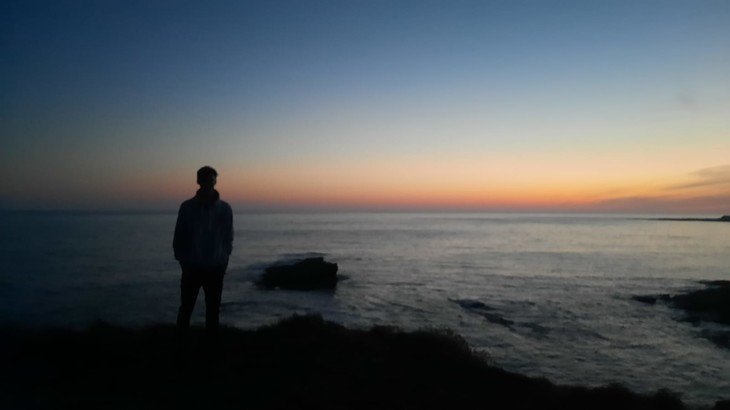 Mathis steht im Sonnenuntergang am Meer